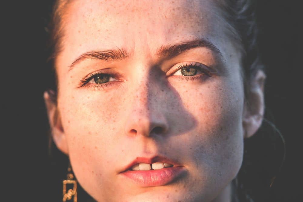 A woman in her early thirties with freckled, sunlit skin — honest texture in warm natural light