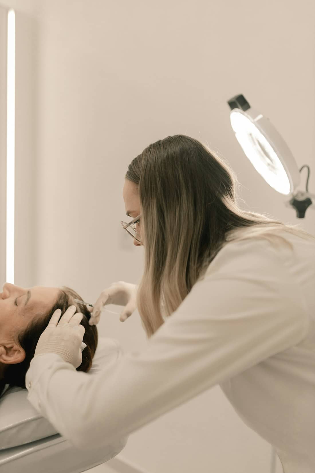 A practitioner in white gloves placing a precise neurotoxin injection near a client's brow in soft natural light