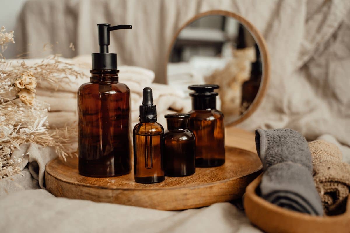 Unlabeled amber-glass apothecary bottles on a wooden tray beside folded linen